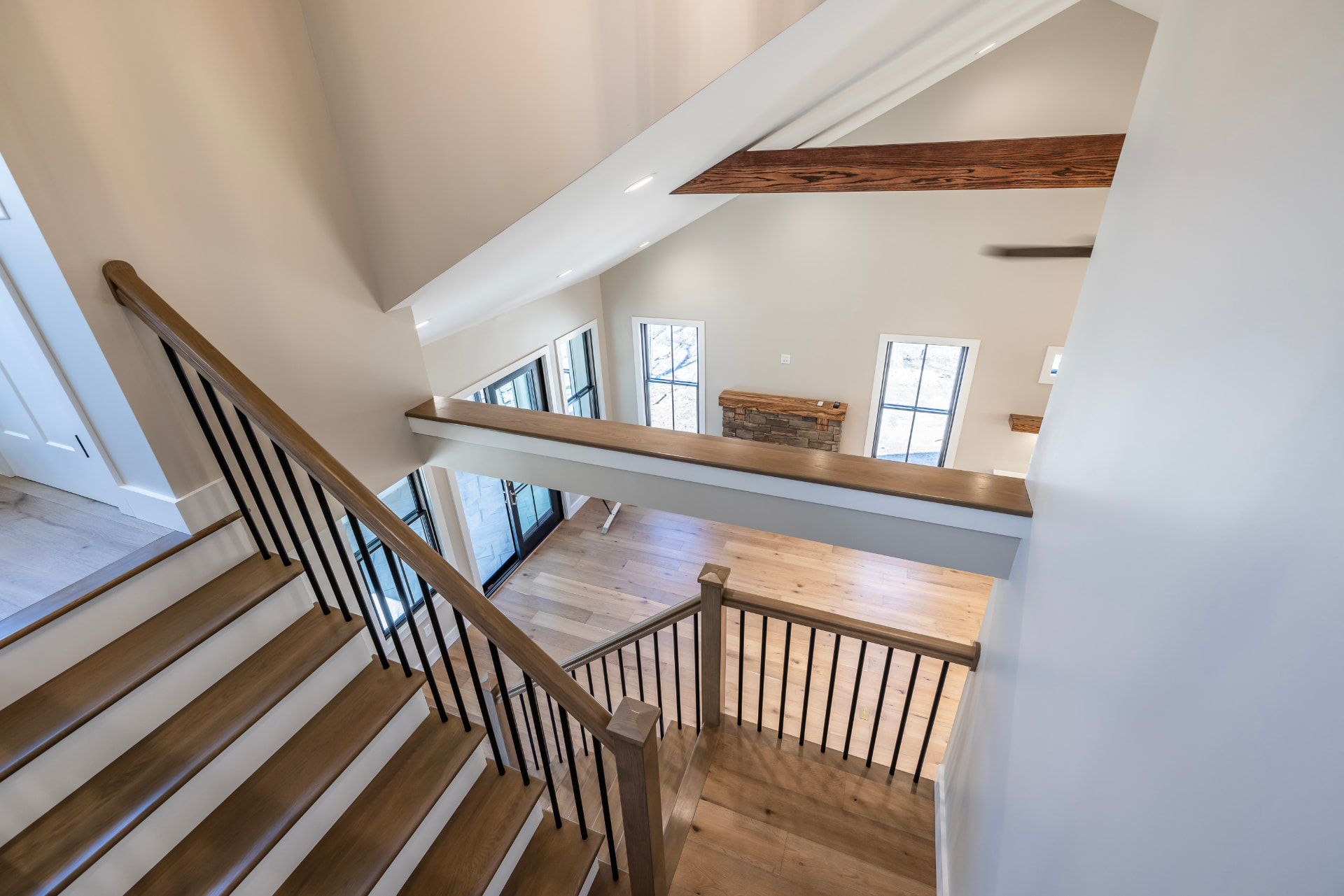 Oak staircase with black balusters overlooking the great room and stone fireplace