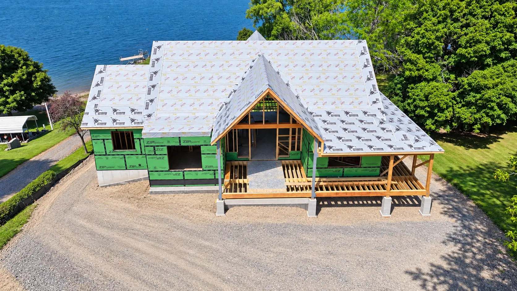 Aerial view of the lakefront home under construction with ZIP sheathing, roof underlayment, and the lake behind